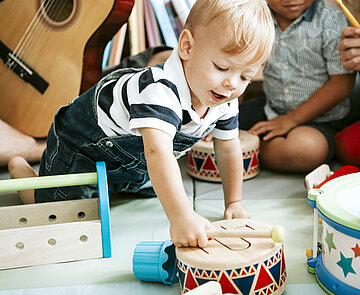 Little kid playing with a wooden drum set